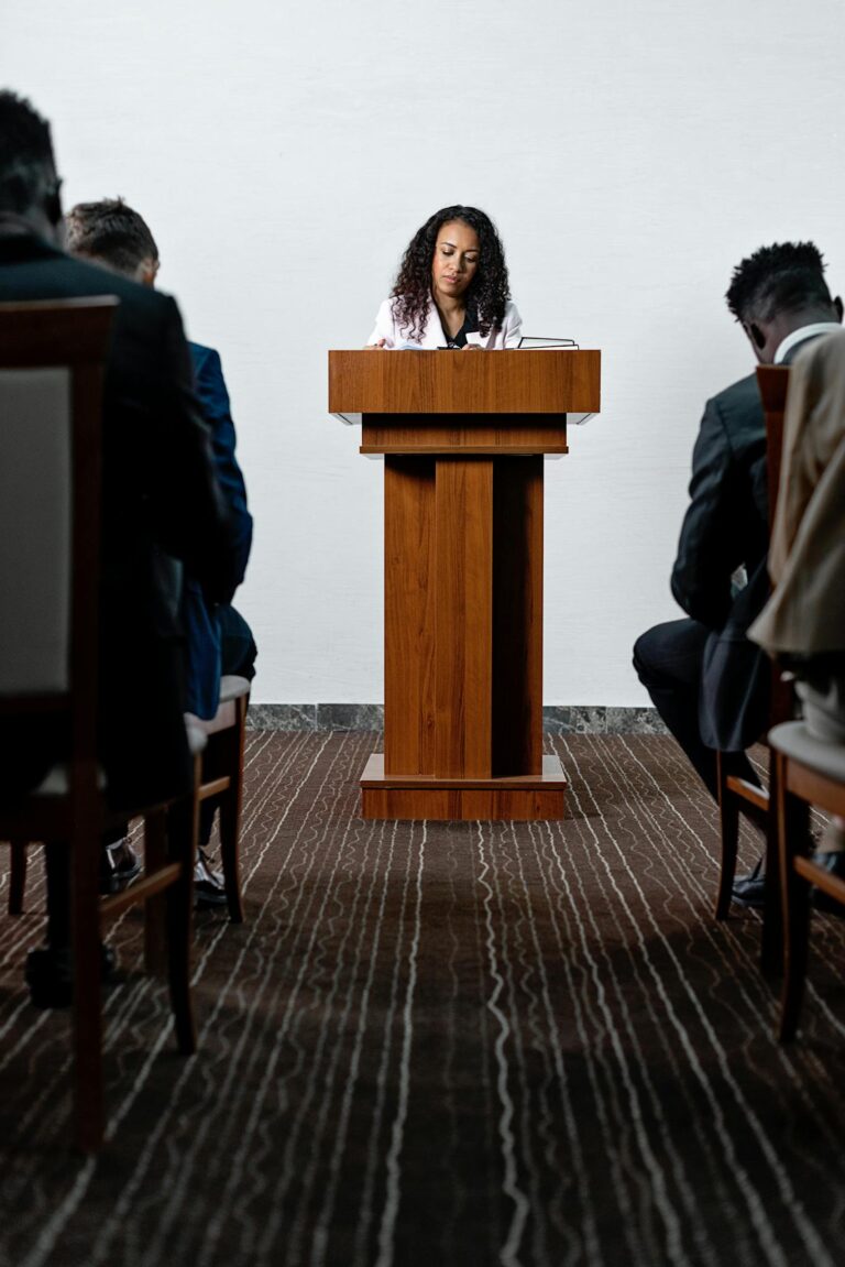 James Bleier Woman delivering a speech at a conference with attendees seated.